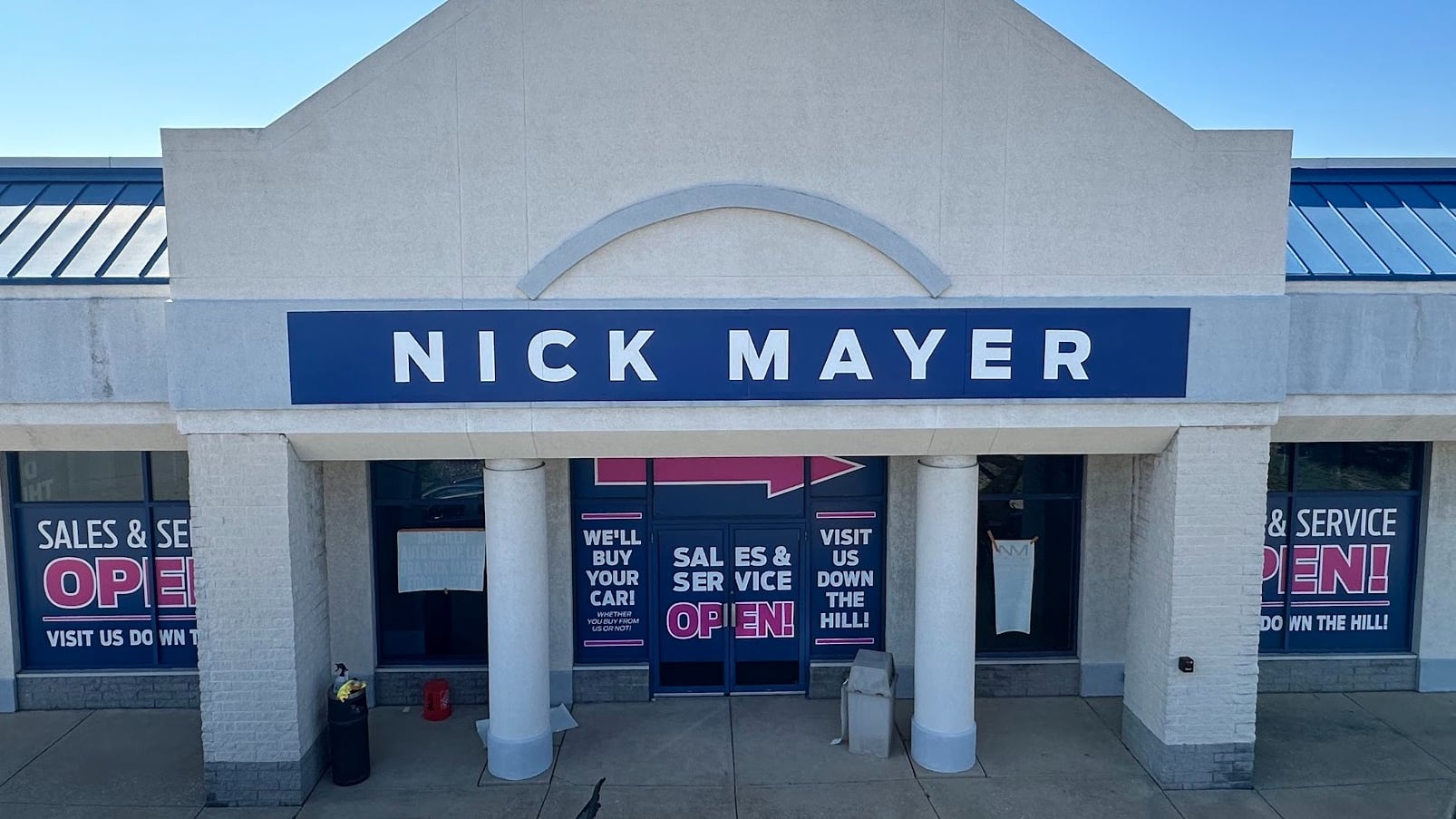 A white automotive dealership with red, white and blue signs.